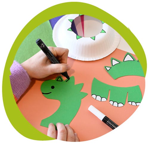 Person zeichnet Dino-Kopf Schablone auf grünes Tonpapier ab