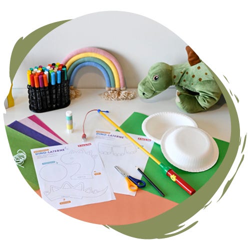 Ausgedruckte Bastelvorlage, Pappteller, Tonpapier, Transparentpapier, Laternenstab, Schere, Kleber und Stifte liegen auf einem Tisch