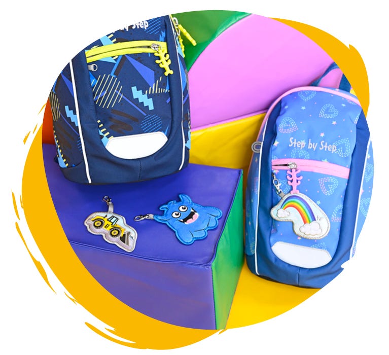 Bunte Kindergartenrucksäcke liegen nebeneinander vor einer bunten Wand