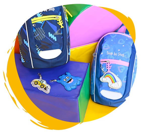 Bunte Kindergartenrucksäcke liegen nebeneinander vor einer bunten Wand