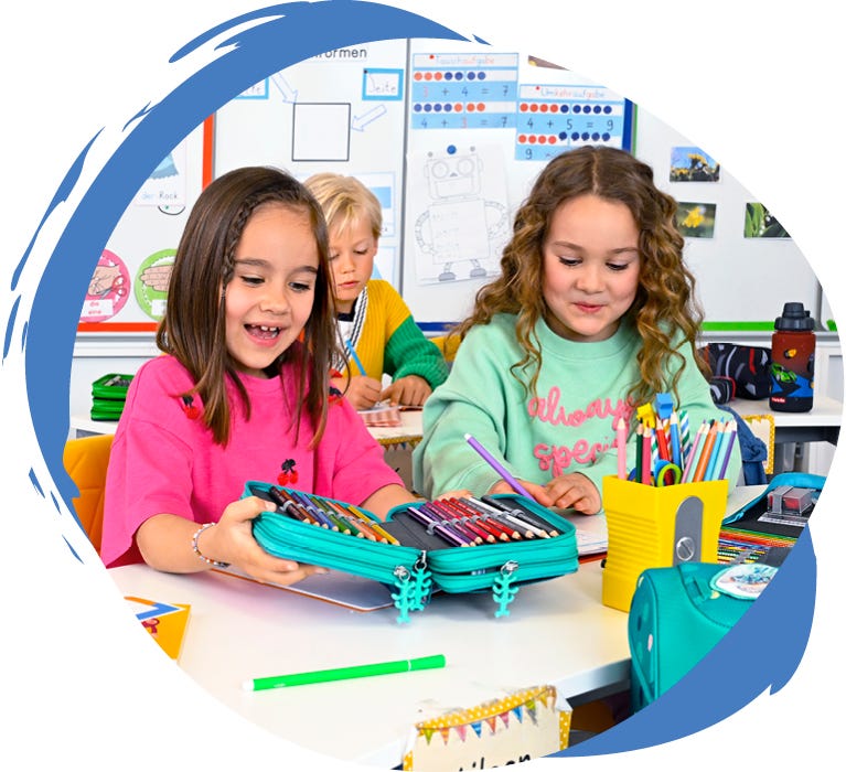 Kinder im Klassenzimmer mit ge&ouml;ffnetem Sch&uuml;leretui voller Buntstifte und weiteren Schulmaterialien auf dem Tisch.