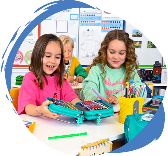 Kinder im Klassenzimmer mit ge&ouml;ffnetem Sch&uuml;leretui voller Buntstifte und weiteren Schulmaterialien auf dem Tisch.