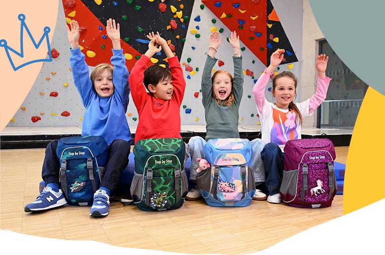 Vier Kinder mit Schulrucks&auml;cken vor einer Kletterwand in der Sporthalle. Modelle mit Weltraum-, Dinosaurier-, Axolotl- und Einhornmotiven.