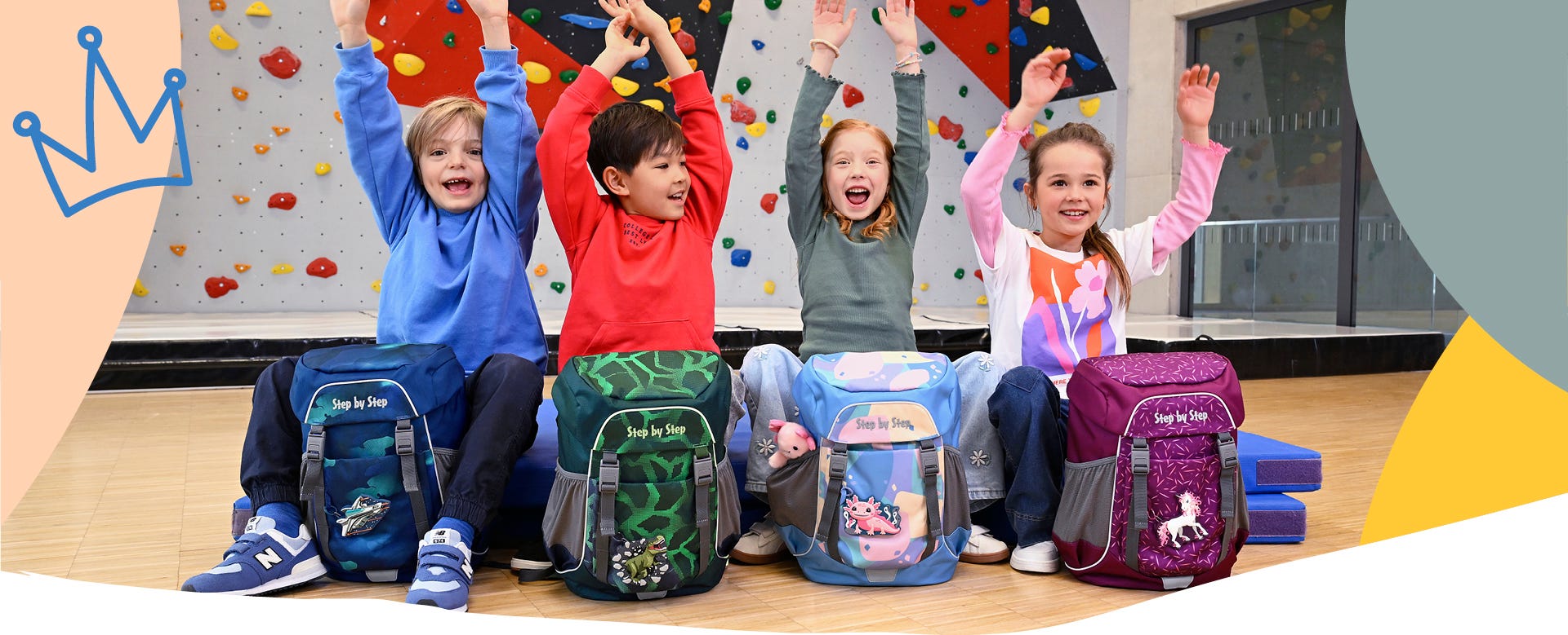 Vier Kinder mit Schulrucks&auml;cken vor einer Kletterwand in der Sporthalle. Modelle mit Weltraum-, Dinosaurier-, Axolotl- und Einhornmotiven.