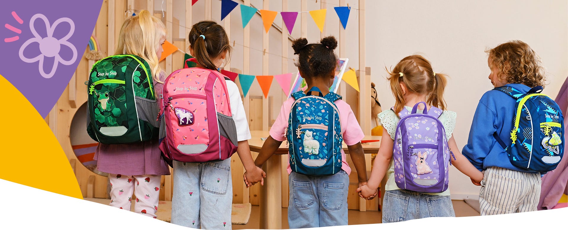 Fünf Kinder mit unterschiedlich gestalteten Kindergartenrucksäcken stehen Hand in Hand in einem Gruppenraum.