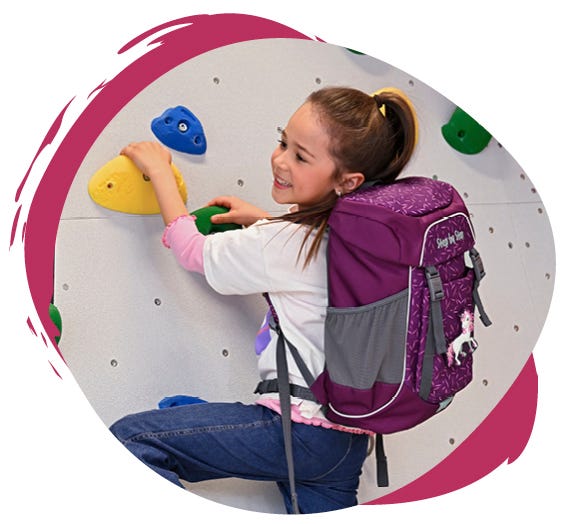 ACTIVE Kind klettert mit violettem Rucksack mit Einhornmotiv an einer Kletterwand mit bunten Griffen.