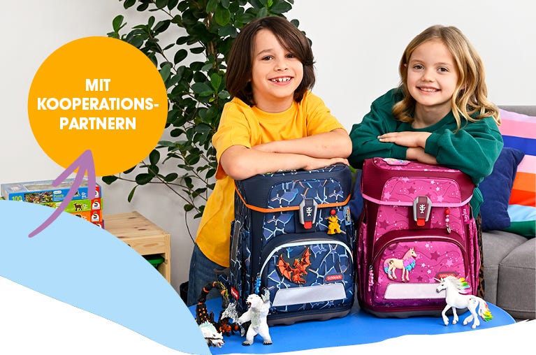 Zwei Kinder pr&auml;sentieren Schulranzen mit Drachen- und Einhornmotiven in einem Wohnraum. Text: &sbquo;Mit Kooperationspartnern&lsquo;