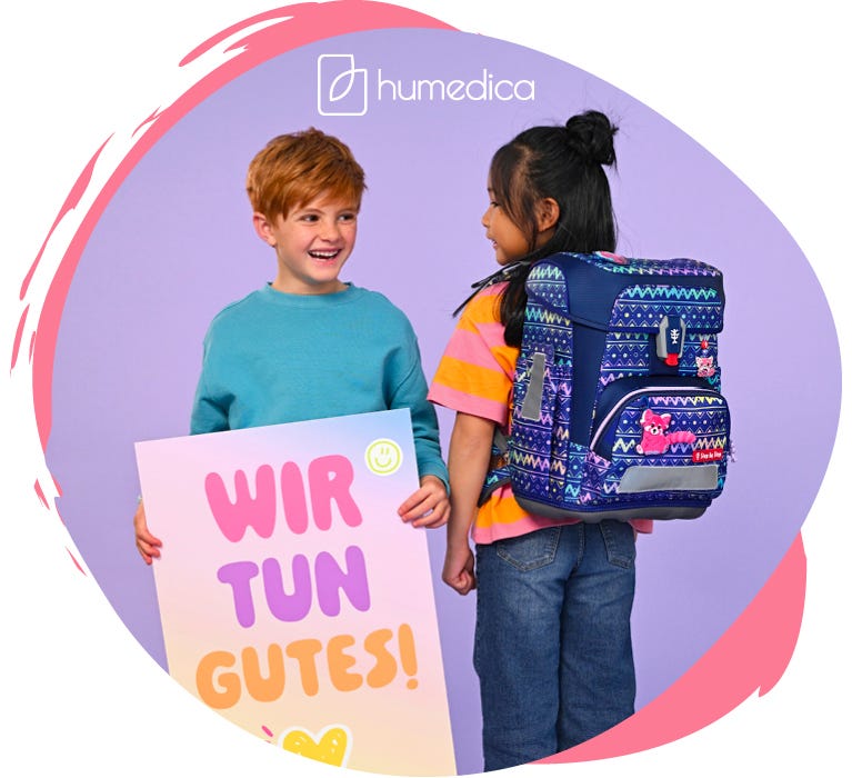 zwei Kinder pr&auml;sentieren einen bunt gemusterten Schulranzen mit einem pinken Panda als Frontmotiv