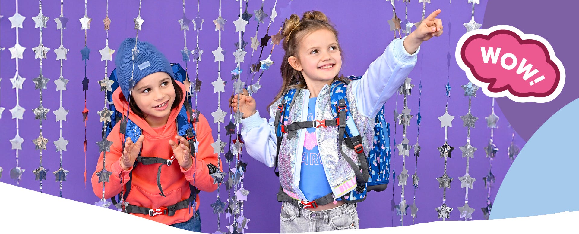 Zwei Kinder mit blauen Schulrucks&auml;cken vor violettem Hintergrund mit Sternengirlanden. Text: &sbquo;WOW!&lsquo;.