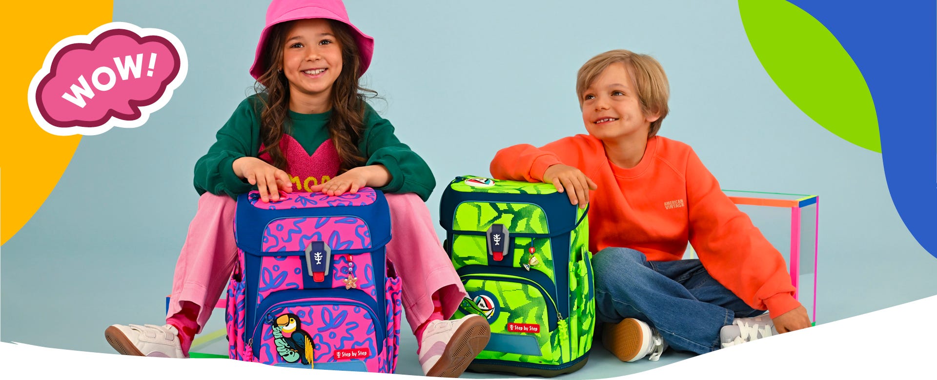 Zwei Kinder pr&auml;sentieren einen pink-blauen und einen neongr&uuml;n-blauen Schulranzen im Neon-Design. Text: &sbquo;WOW!&lsquo;.