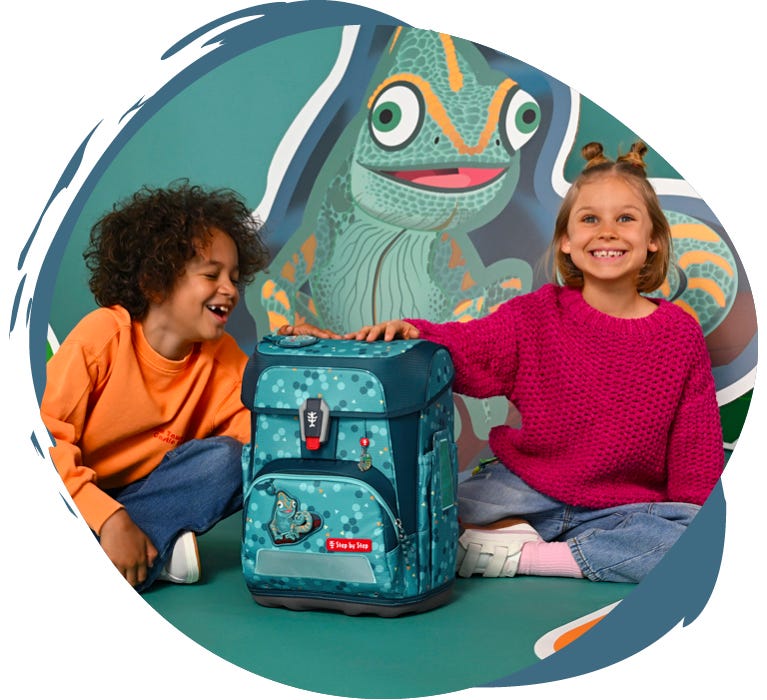Zwei Kinder pr&auml;sentieren einen hellblauen Schulranzen mit Cham&auml;leon-Motiv vor einer gro&szlig;en Cham&auml;leon-Illustration.