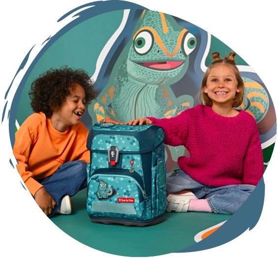 Zwei Kinder pr&auml;sentieren einen hellblauen Schulranzen mit Cham&auml;leon-Motiv vor einer gro&szlig;en Cham&auml;leon-Illustration.