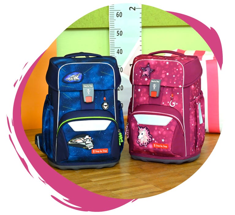 Zwei Schulranzen auf einem Holztisch: links ein blauer mit Weltraum-Motiv, rechts ein pinker mit Einhorn- und Sternen-Design.