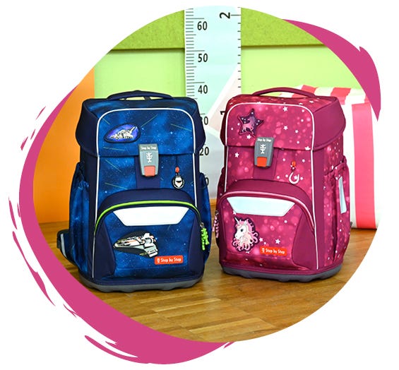 Zwei Schulranzen auf einem Holztisch: links ein blauer mit Weltraum-Motiv, rechts ein pinker mit Einhorn- und Sternen-Design.