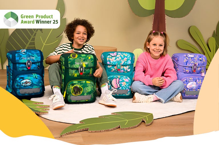 Zwei Kinder pr&auml;sentieren vier Schulranzen in verschiedenen Designs. Hinweis: &sbquo;Green Product Award Winner 25&lsquo;.