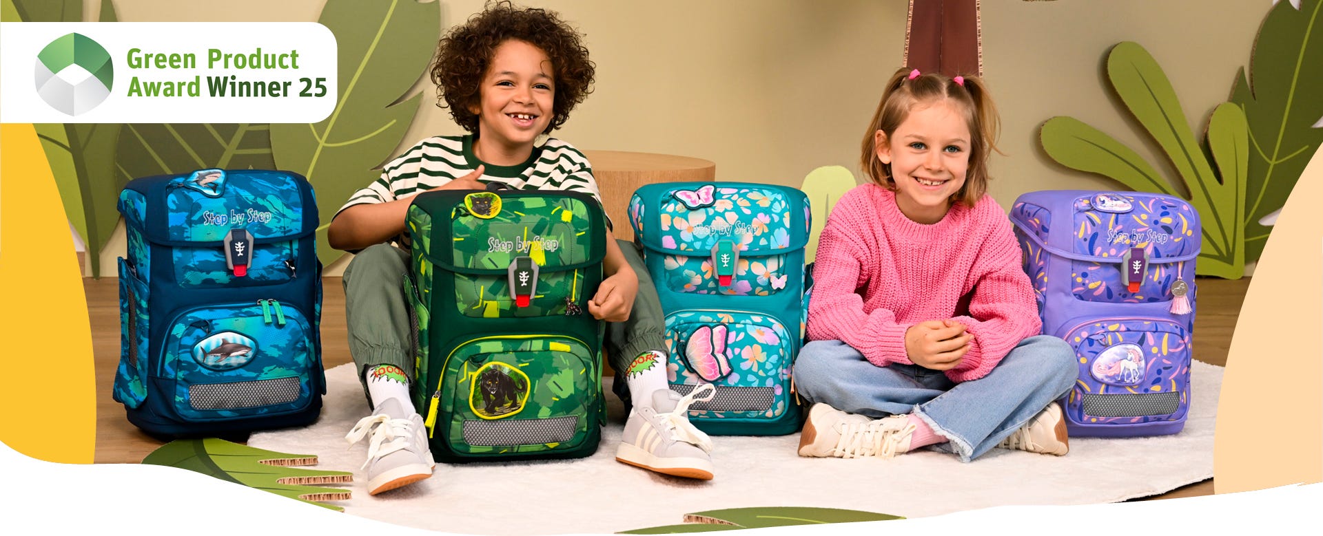 Zwei Kinder pr&auml;sentieren vier Schulranzen in verschiedenen Designs. Hinweis: &sbquo;Green Product Award Winner 25&lsquo;.