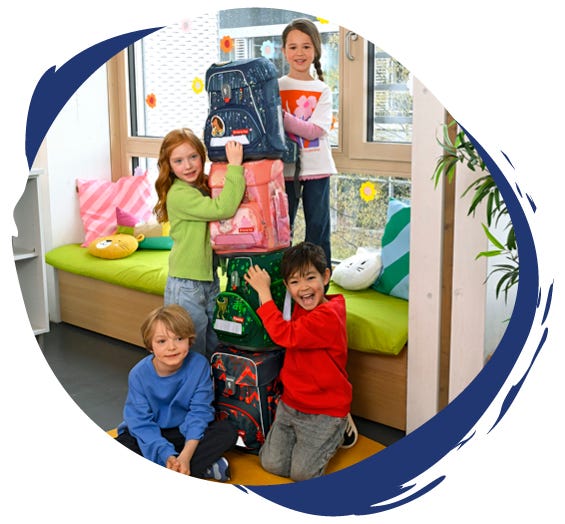 Vier Kinder präsentieren einen Stapel aus Schulranzen mit Pferde-, Hunde-, Dinosaurier- und Drachenmotiven.