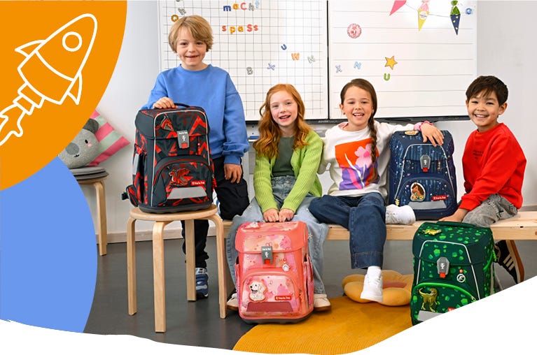 Vier Kinder präsentieren Schulranzen mit Drachen-, Hunde-, Weltraum- und Dinosauriermotiven im Klassenzimmer.